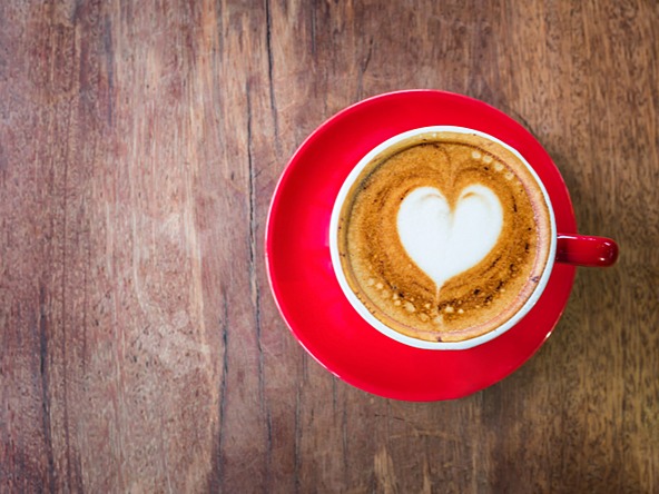 coffee in a red cup and saucer, with a heart shape in the steamed milk 